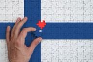 A hand placing the final piece into a jigsaw puzzle of the Finnish flag.