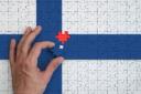 A hand placing the final piece into a jigsaw puzzle of the Finnish flag.