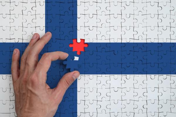 A hand placing the final piece into a jigsaw puzzle of the Finnish flag.
