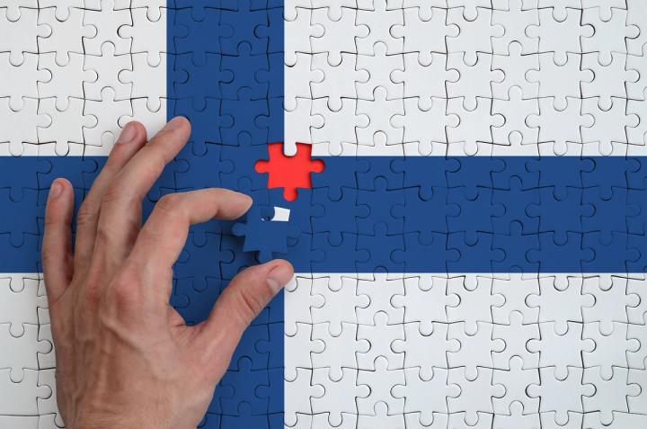 A hand placing the final piece into a jigsaw puzzle of the Finnish flag.