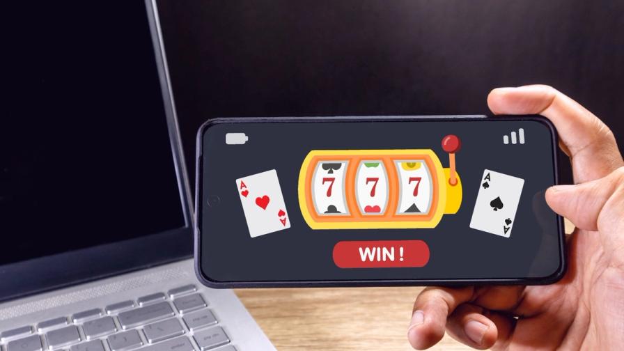 A hand holding a smartphone displaying an online casino game with a slot machine showing triple sevens and a