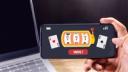 A hand holding a smartphone displaying an online casino game with a slot machine showing triple sevens and a