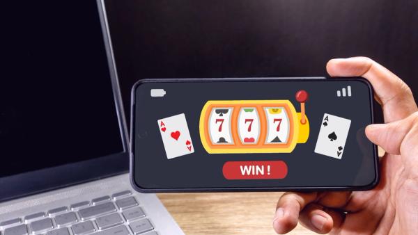 A hand holding a smartphone displaying an online casino game with a slot machine showing triple sevens and a