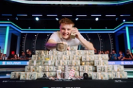 Lucas Jumalon smiles behind a massive pyramid of cash, holding a stack to his ear and displaying his WSOP championship bracelet.