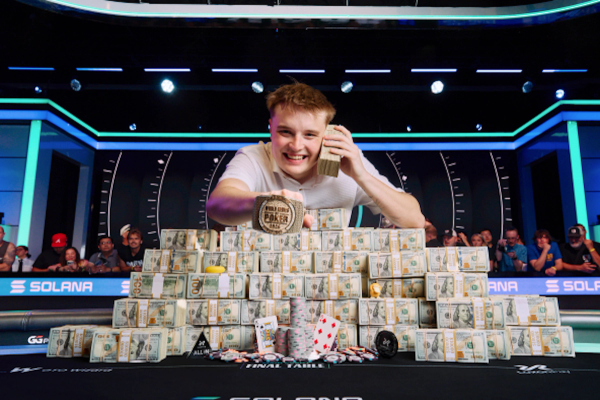 Lucas Jumalon smiles behind a massive pyramid of cash, holding a stack to his ear and displaying his WSOP championship bracelet.