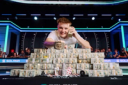 Lucas Jumalon smiles behind a massive pyramid of cash, holding a stack to his ear and displaying his WSOP championship bracelet.
