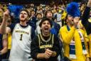 Excited Michigan sports fans cheering and shouting in a crowded stadium, waving blue pom-poms.