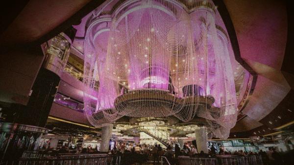 A massive, glowing purple beaded chandelier hanging over a multi-level bar inside a casino.