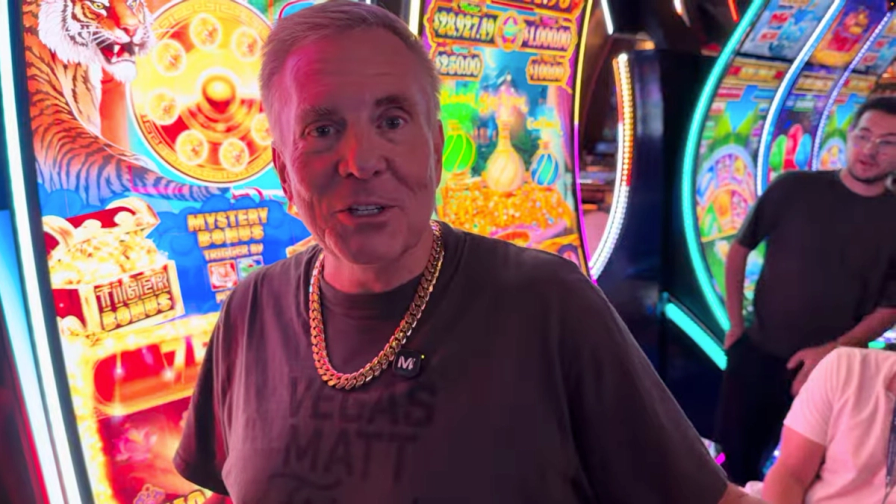 Vegas Matt wearing a gold chain and standing in front of colorful slot machines in a casino.