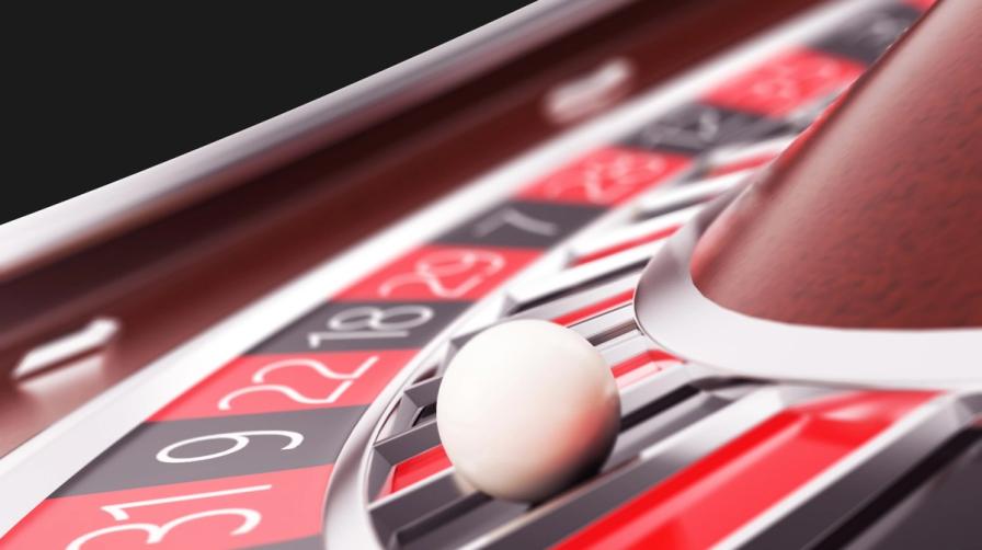 Close-up of a white ball resting on a casino roulette wheel with red and black numbered pockets.