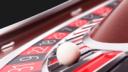 Close-up of a white ball resting on a casino roulette wheel with red and black numbered pockets.