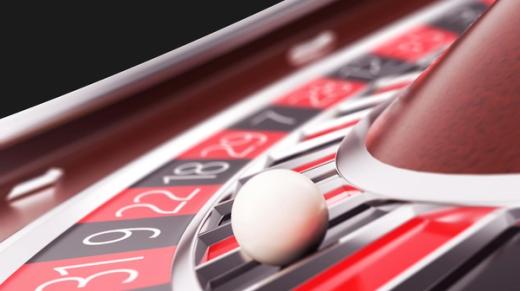 Close-up of a white ball resting on a casino roulette wheel with red and black numbered pockets.