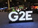 A large, glowing white G2E sign on a convention floor with casino gaming booths in the background.