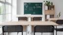 An empty classroom with wooden desks, black chairs, and a green chalkboard in the background reading Back to