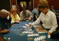 A dealer in a white shirt deals cards to players seated around a blue blackjack table at a casino.
