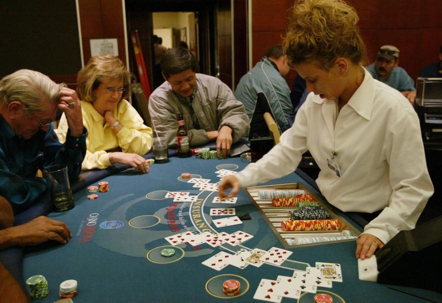 A dealer in a white shirt deals cards to players seated around a blue blackjack table at a casino.