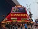 Bright red neon lights of the Fremont Casino in downtown Las Vegas, with a large digital billboard and pedestrians