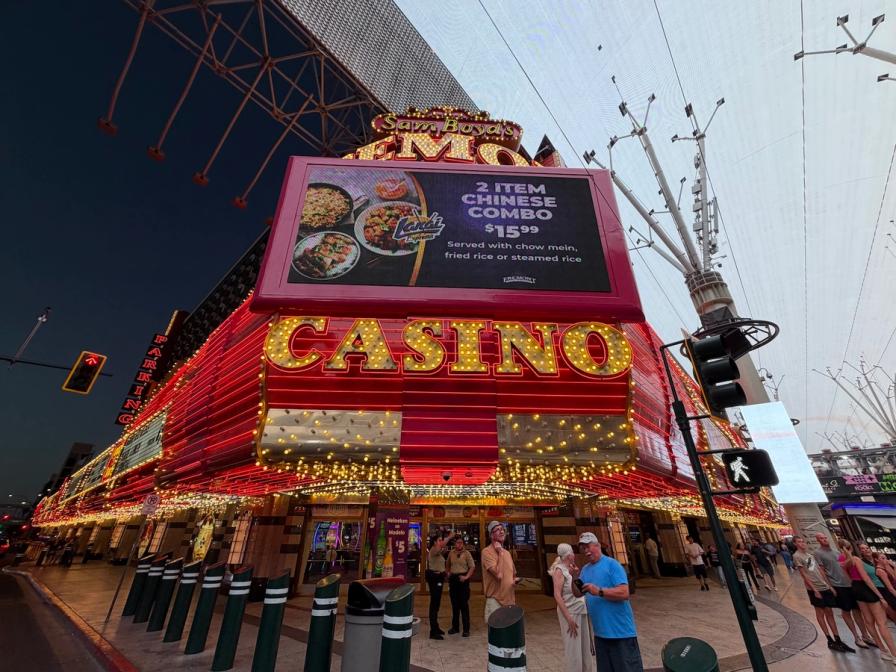 Bright red neon lights of the Fremont Casino in downtown Las Vegas, with a large digital billboard and pedestrians