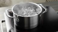 A stainless steel pot of boiling water with steam rising on a black induction cooktop.