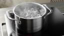 A stainless steel pot of boiling water with steam rising on a black induction cooktop.