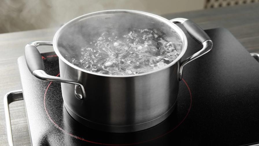 A stainless steel pot of boiling water with steam rising on a black induction cooktop.