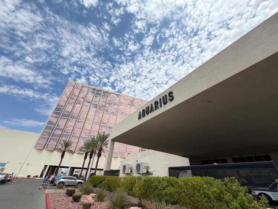 Low-angle view of the Aquarius hotel building with pink reflective windows under a blue sky filled with wispy white clouds.