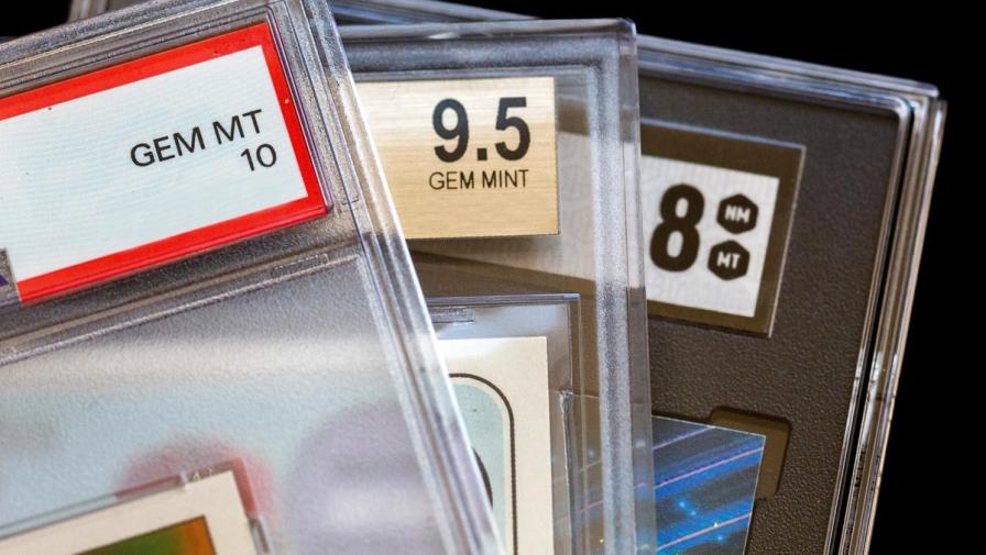 Close-up of three graded trading cards in plastic slabs, showing grades of GEM MT 10, 9.5 GEM MINT, and 8 NM MT.