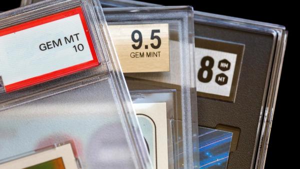Close-up of three graded trading cards in plastic slabs, showing grades of GEM MT 10, 9.5 GEM MINT, and 8 NM MT.
