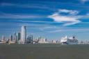 A cruise ship sails past the Jersey City skyline on a sunny day.