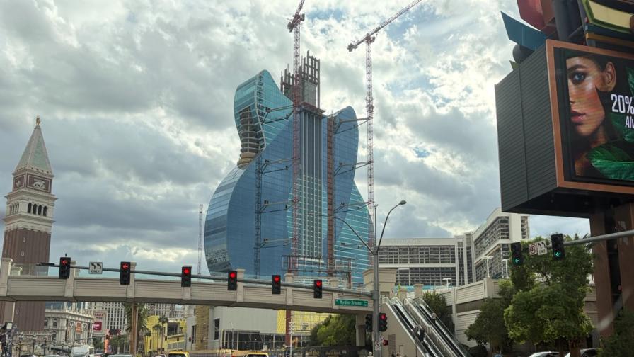 A blue, guitar-shaped hotel tower under construction with cranes in Las Vegas.