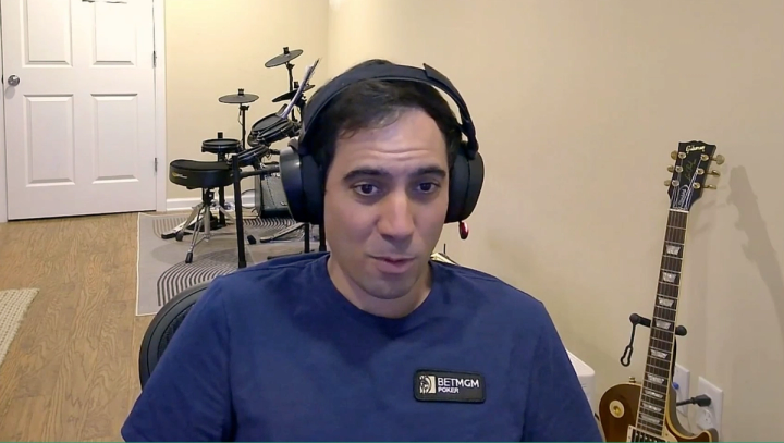 Michael Gagliano wearing headphones and a BetMGM Poker shirt, with a drum kit and electric guitar in the background.