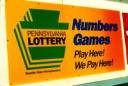 Yellow and orange Pennsylvania Lottery sign reading "Numbers Games Play Here! We Pay Here!
