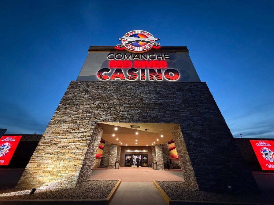 Illuminated entrance of the Comanche Red River Casino with a large stone facade under a twilight sky.