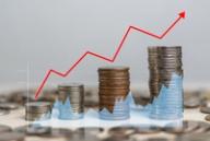 Four stacks of coins of increasing height overlaid with a rising red arrow graph and a blue area chart.