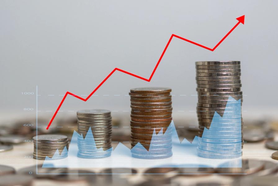 Four stacks of coins of increasing height overlaid with a rising red arrow graph and a blue area chart.