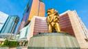 A large golden lion statue stands in front of a modern MGM resort building under a clear blue sky.
