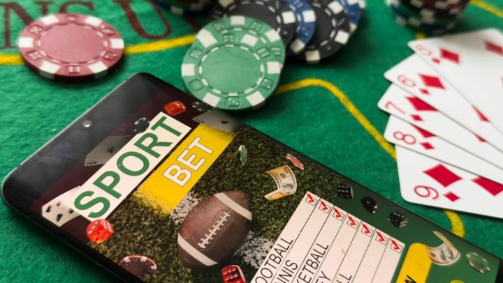 A smartphone displaying a sports betting app on a green casino table next to poker chips and playing cards.