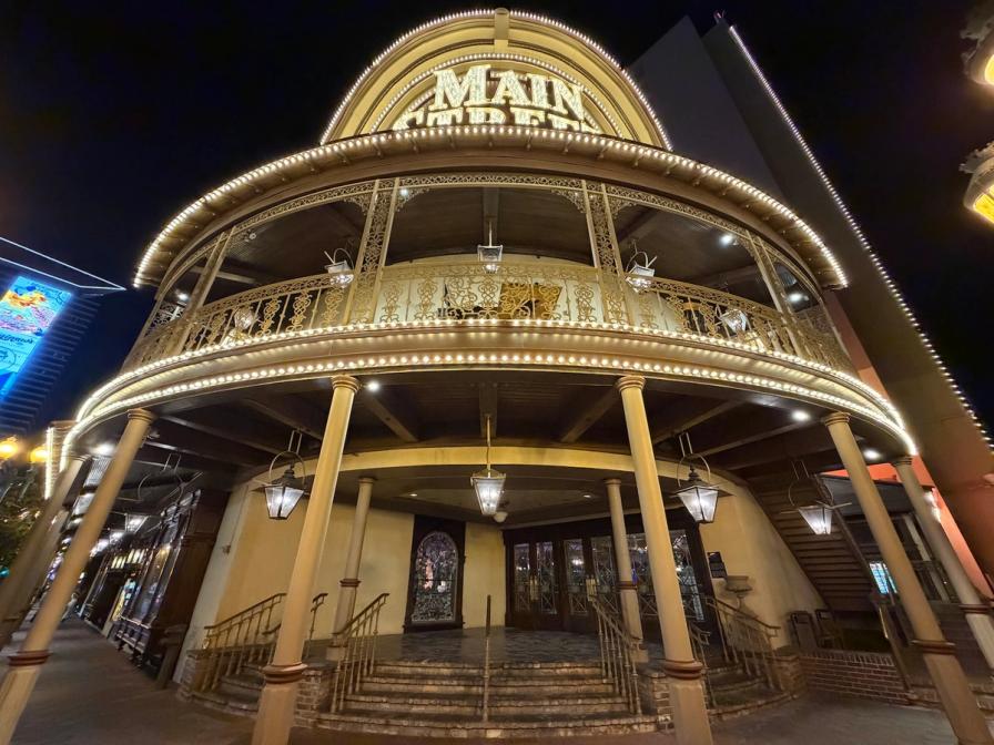 Low-angle night view of the illuminated Victorian-style entrance to Main Street Station, featuring curved balconies and warm lights.