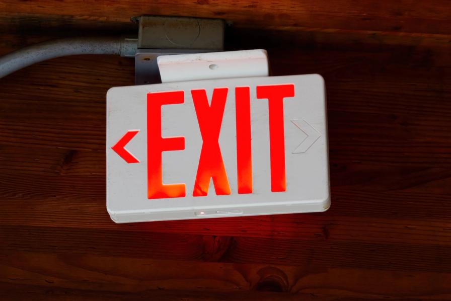 An illuminated red and white exit sign mounted on a wooden ceiling.