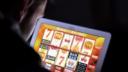 Over-the-shoulder view of a person playing an online slot machine game on a tablet in a dark room.