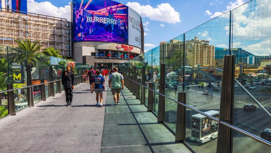 Pedestrians walking on an elevated glass-walled walkway on the Las Vegas Strip.