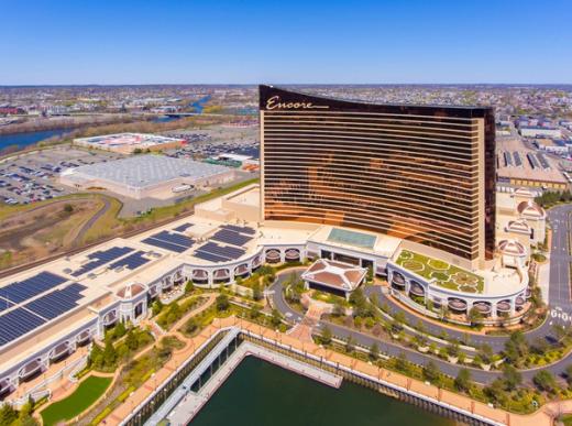 Aerial view of the Encore Boston Harbor resort, a curved bronze-glass hotel tower next to a waterfront.