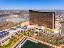 Aerial view of the Encore Boston Harbor resort, a curved bronze-glass hotel tower next to a waterfront.