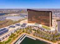 Aerial view of the Encore Boston Harbor resort, a curved bronze-glass hotel tower next to a waterfront.