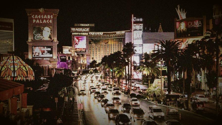 Heavy traffic on the Las Vegas Strip at night, lined with palm trees and glowing casino signs like Caesars Palace and The Mirage.