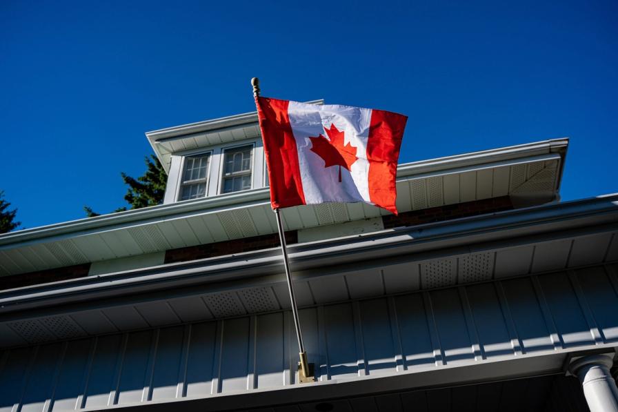 A Canadian flag flying from a flagpole on a house against a clear blue sky.