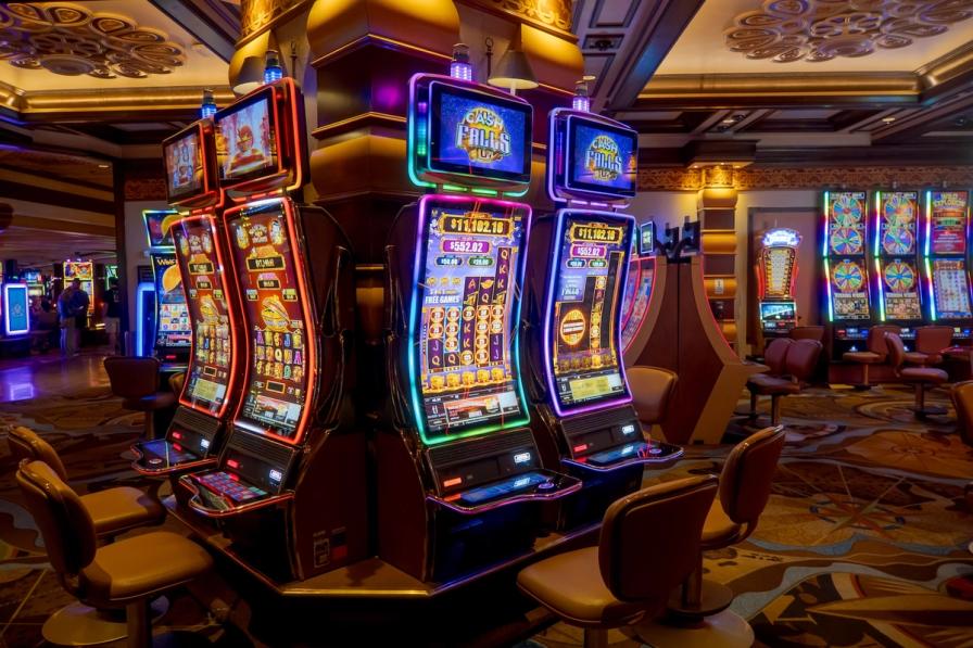 Brightly lit modern slot machines with neon borders and empty chairs on a casino floor.