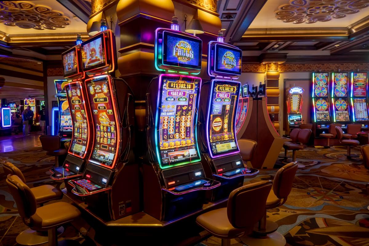 Brightly lit modern slot machines with neon borders and empty chairs on a casino floor.