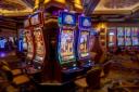 Brightly lit modern slot machines with neon borders and empty chairs on a casino floor.