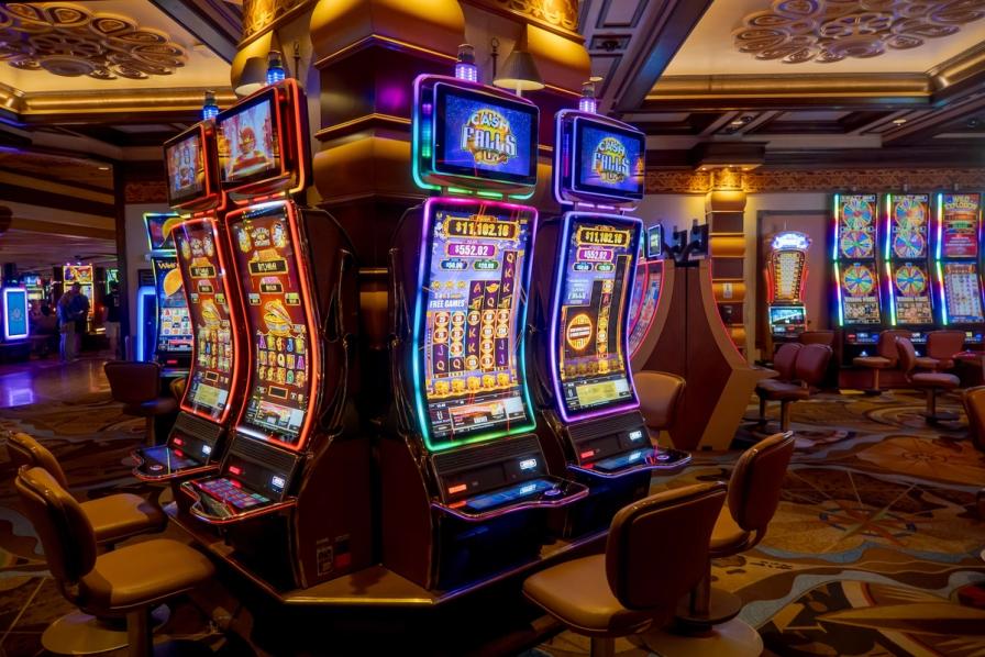 Brightly lit modern slot machines with neon borders and empty chairs on a casino floor.